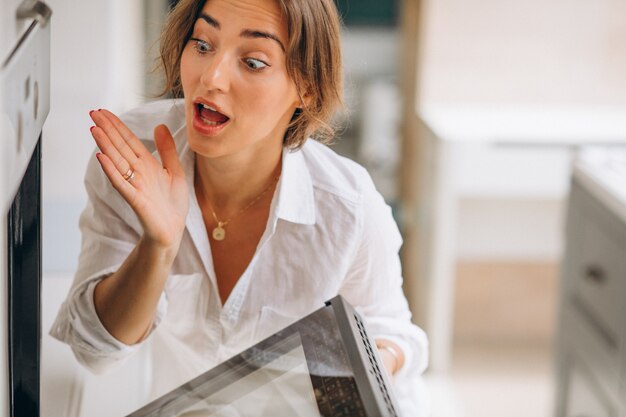 Mulher assando na cozinha e olhando para o forno