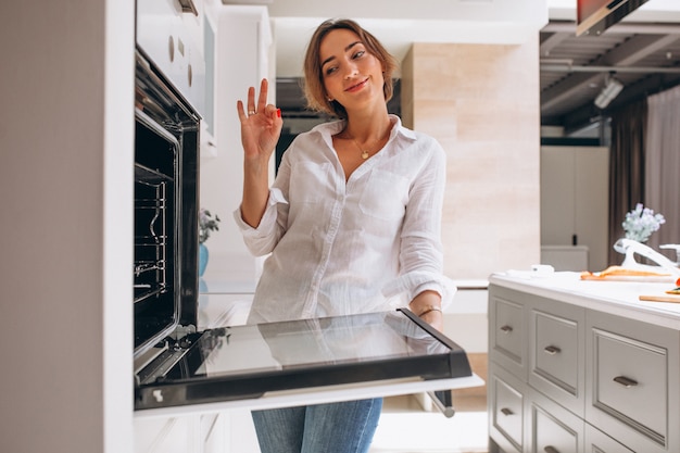 Mulher assando na cozinha e olhando para o forno