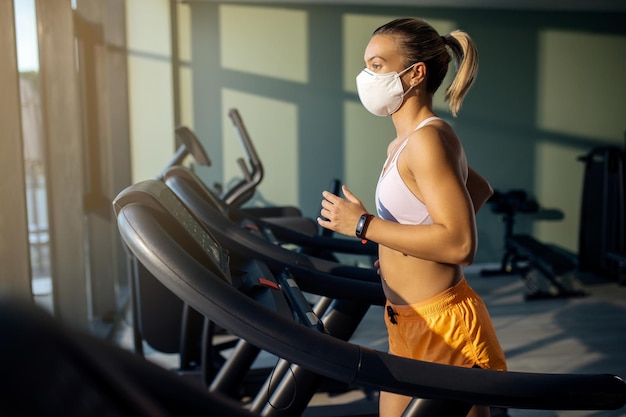 Mulher atlética com máscara facial correndo na esteira no health club