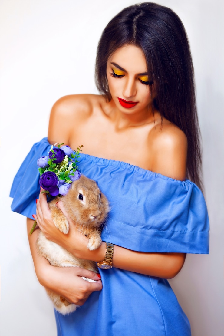 Foto grátis mulher atraente com longos cabelos castanhos, belos olhos, lábios vermelhos e pele perfeita posando no estúdio em um vestido azul com coelho e flores