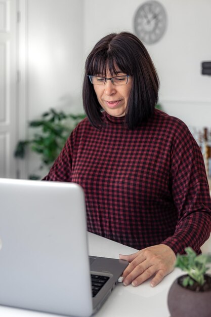 Mulher atraente de meia-idade trabalhando em um laptop enquanto está sentado em uma mesa