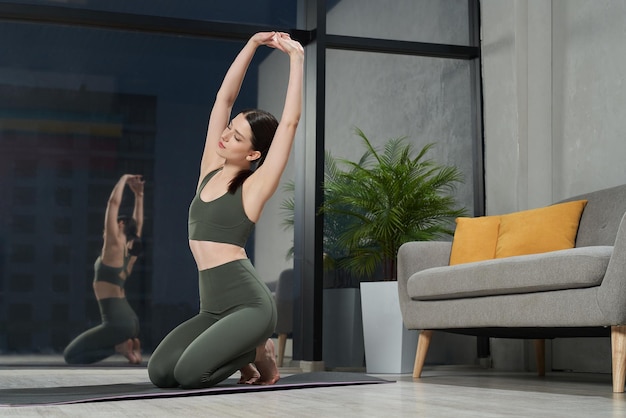 Mulher atraente e flexível sentada descalça no tapete de ioga.