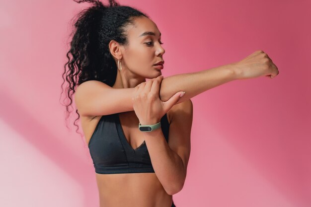 Mulher atraente em legging preta e roupa de ginástica top na parede rosa isolada