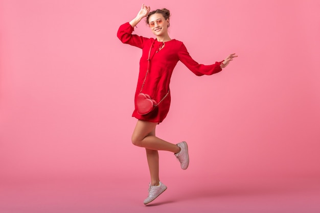 Mulher atraente, feliz e sorridente elegante em um vestido vermelho da moda, pulando correndo na parede rosa isolada, tendência da moda primavera-verão, humor romântico garota glamour