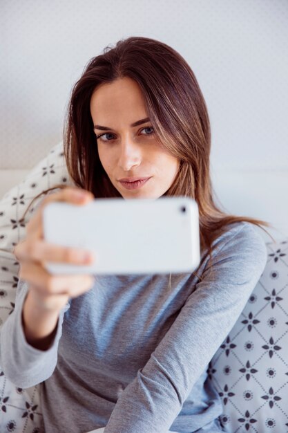 Mulher atraente que leva selfie na cama