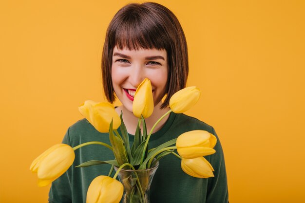 Mulher atraente rindo e segurando flores. Retrato de meninas muito morenas, expressando felicidade com tulipas.