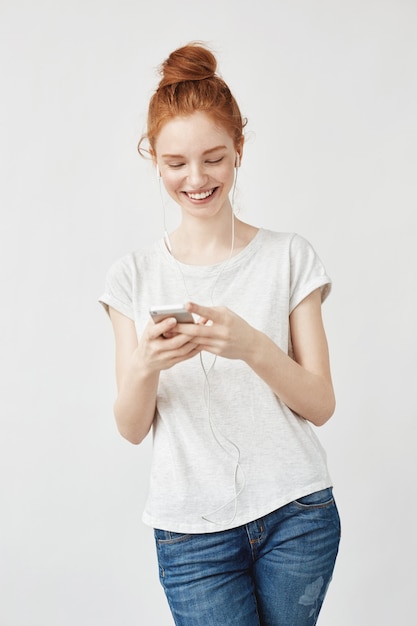 Mulher atraente ruiva com sardas sorrindo olhando para celular.