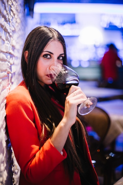 Mulher bebendo vinho e apoiando-se na parede