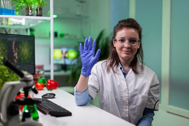 Mulher bioquímica cumprimentando o cientista remoto discutindo o teste de experimento de microbiologia durante a conferência de videochamada online. Médico pesquisador trabalhando em laboratório biológico. Teleconferência