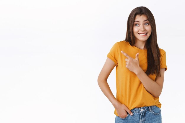 Mulher boba e sedutora como um vestido de loja, mordendo o lábio e sorrindo, parece fascinada e interessada, apontando olhando para a esquerda, rosto ansioso, pedindo para namorada comprar com uma expressão inocente