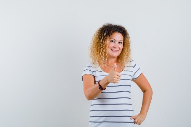 Mulher bonita aparecendo o polegar em t-shirt e olhando positiva, vista frontal.