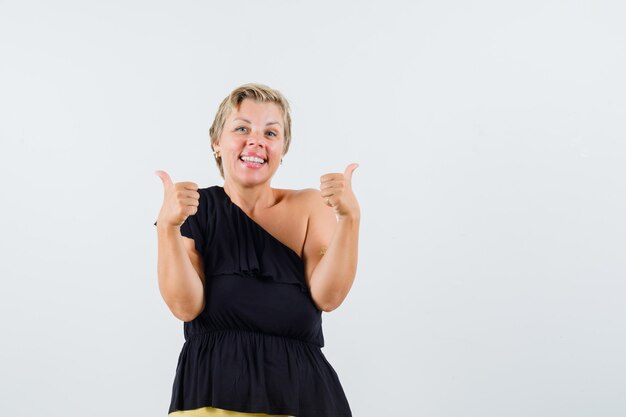 Mulher bonita aparecendo o polegar na blusa preta e parecendo satisfeita.