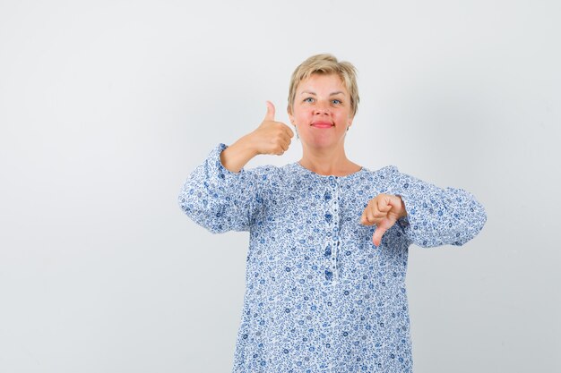 Mulher bonita, apontando para cima e para baixo na blusa estampada e olhando perplexa, vista frontal.