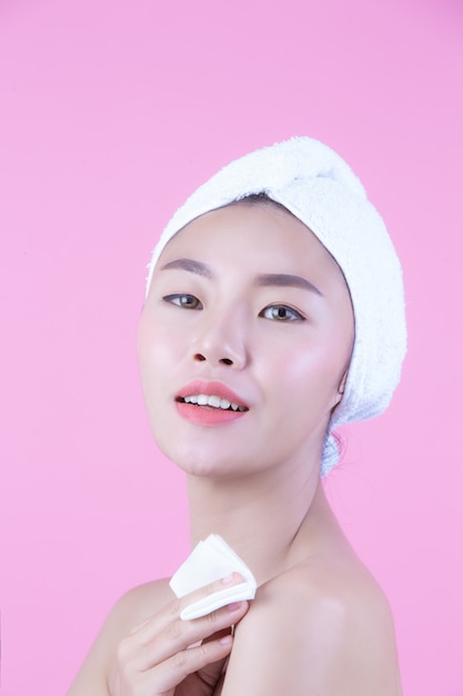 Mulher bonita asiática que limpa a cara em um fundo, em uma cosmetologia e em uns termas cor-de-rosa.