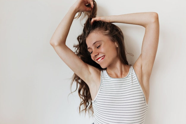 Foto grátis mulher bonita atraente com cabelo comprido ondulado usando camiseta despojada mordendo o lábio e tocando o cabelo na parede isolada