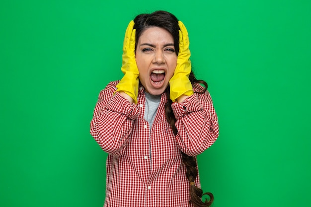 Mulher bonita caucasiana de limpeza irritada com luvas de borracha cobrindo as orelhas e