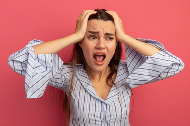 Mulher bonita caucasiana irritada com as mãos na cabeça e olhando para o lado rosa