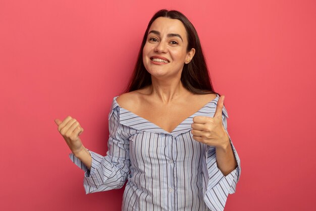 Mulher bonita caucasiana sorridente com o polegar para cima e apontando para o lado isolado