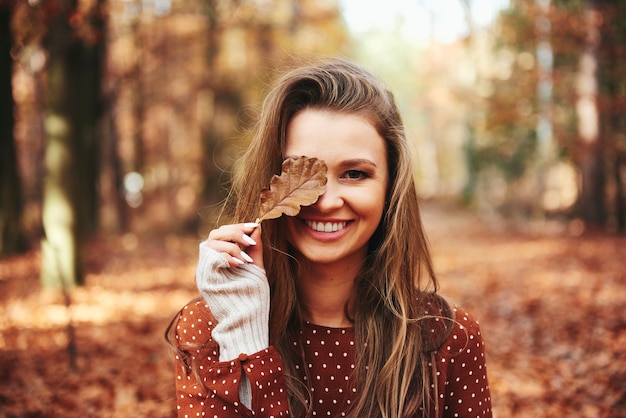 Mulher bonita cobrindo os olhos com folhas outonais