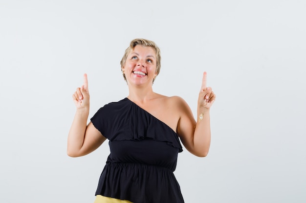 Mulher bonita com blusa preta apontando para cima e parecendo divertida