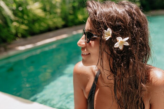 Mulher bonita com cabelo comprido molhado na piscina. Garota européia bronzeada, rosto lindo, aproveitando o verão em um dia quente no resort tropical