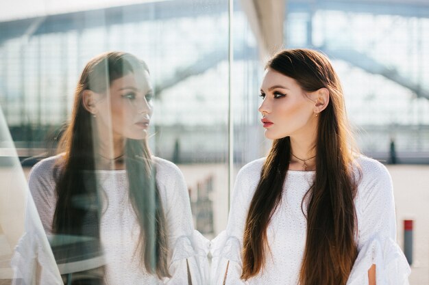 Mulher bonita com cabelo comprido olha para seu reflexo no moderno edifício de vidro