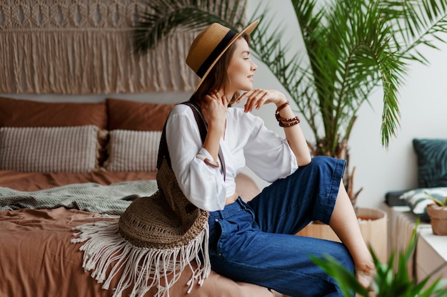 Mulher bonita com cabelos curtos relaxantes no quarto dela, estilo boho, palmeiras e macramê na parede