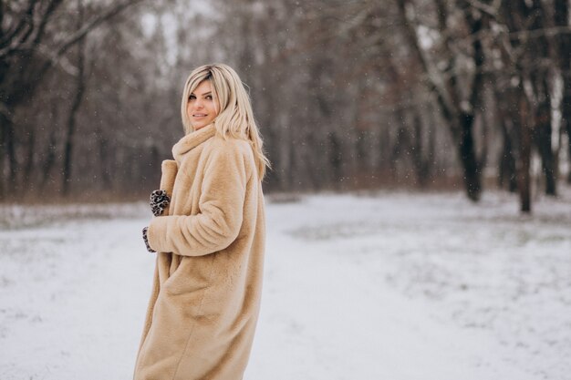 Mulher bonita com casaco de inverno caminhando em um parque cheio de neve