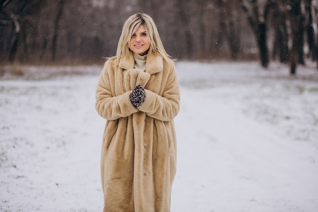 Mulher bonita com casaco de inverno caminhando em um parque cheio de neve