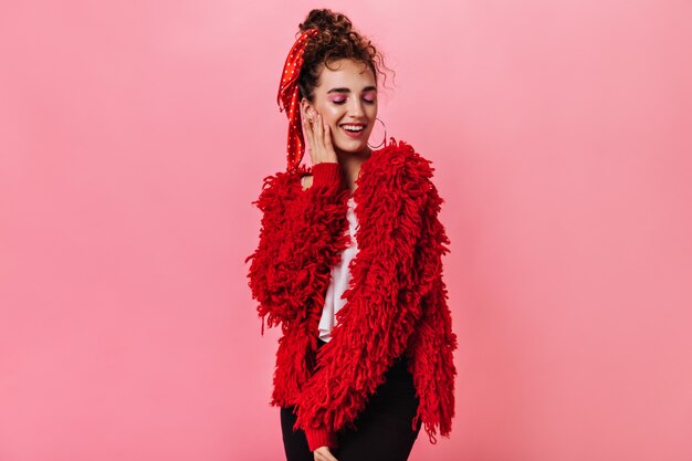 Mulher bonita com casaco vermelho e calça escura posando em rosa