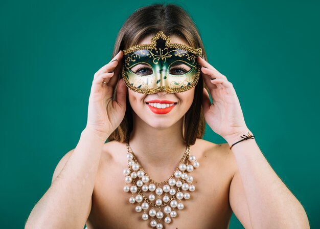Mulher bonita com colar de grânulos e máscara de carnaval em pano de fundo verde