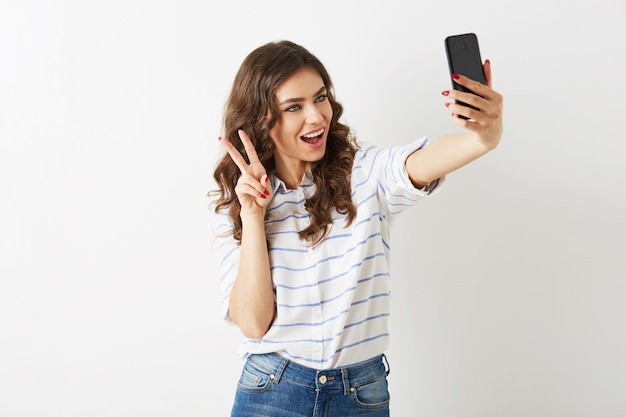Foto grátis mulher bonita com expressão de carinha engraçada fazendo selfie no celular, sorrindo, feliz, desalinhada, cabelo cacheado, humor positivo, estilo estudante hipster