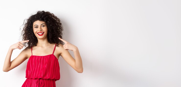 Foto grátis mulher bonita com maquiagem de penteado encaracolado e vestido vermelho apontando para si mesma sorrindo com camiseta branca