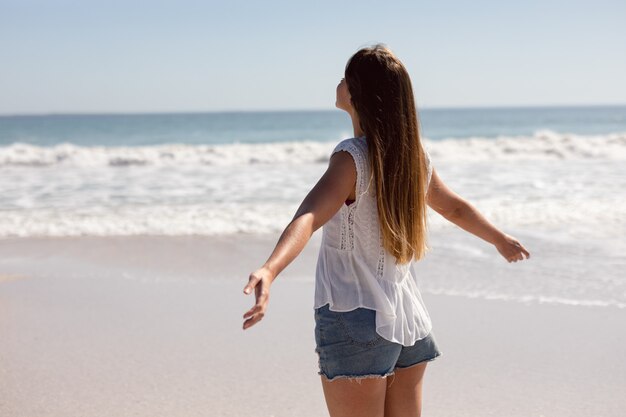 Mulher bonita com os braços esticados em pé na praia sob o sol