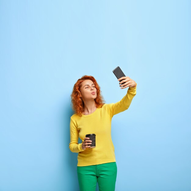 Mulher bonita com os lábios dobrados para a câmera e tira foto em um celular moderno