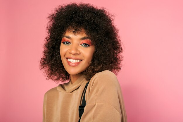 Mulher bonita com pele negra e penteado africano estiloso com roupa esportiva posando em rosa