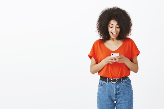 Mulher bonita com penteado afro posando com seu smartphone no estúdio