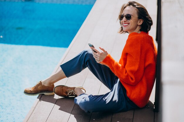 Mulher bonita com telefone sentado à beira da piscina