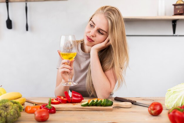 Mulher bonita com um copo e legumes na cozinha