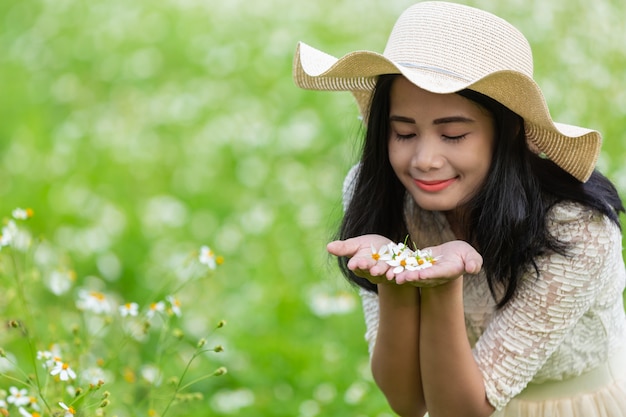 Mulher bonita com um vestido branco bonito, de pé e brincando em um pasto com flores brancas