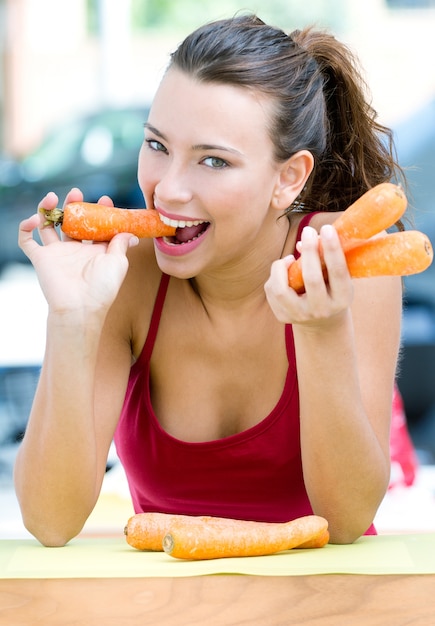 Mulher bonita comendo cenouras em casa