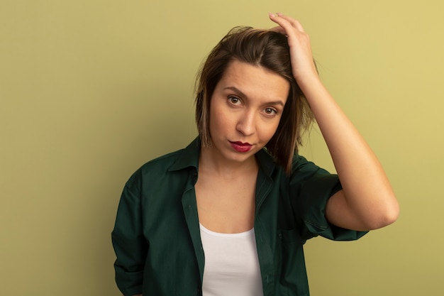 Foto grátis mulher bonita confiante coloca a mão na cabeça, olhando para frente, isolada na parede verde oliva