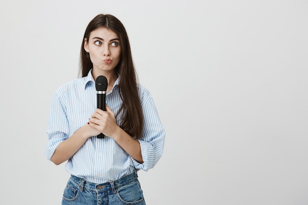 Foto grátis mulher bonita confusa fazendo beicinho pensativo, segurando o microfone