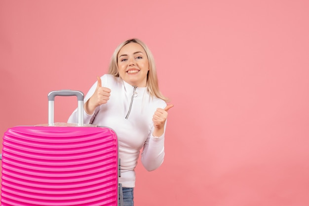 Mulher bonita de frente com mala rosa dando sinal de positivo