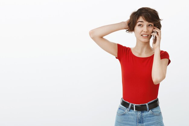 Mulher bonita desajeitada e indecisa coçando a cabeça sem entender enquanto fala ao telefone