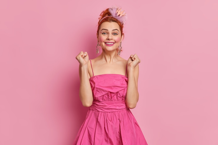 Foto grátis mulher bonita e alegre com cabelo ruivo e maquiagem fecha os punhos alegra algo vestido com um vestido festivo e bandana tem poses de expressão feliz
