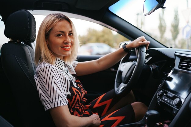 Mulher bonita e confiante em óculos de sol. Retrovisor de mulher jovem e atraente em trajes casuais, dirigindo um carro