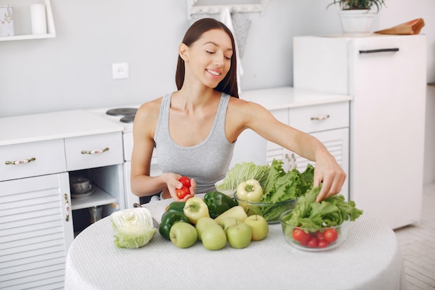 Mulher bonita e desportiva em uma cozinha com legumes