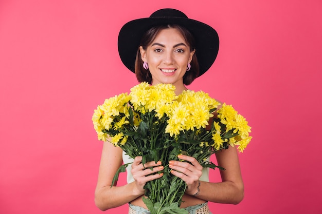 Mulher bonita e elegante posando de chapéu, segurando um grande buquê de ásteres amarelos, clima de primavera, emoções positivas isoladas