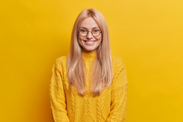 Mulher bonita e feliz com uma expressão alegre sorri e sente-se satisfeita mostra dentes brancos perfeitos, vestida com um macacão casual ouve histórias interessantes ou boas notícias